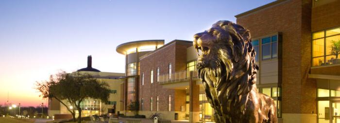 Lion statue in front of a bricked building. It is in the evening and the focus is on the lion.