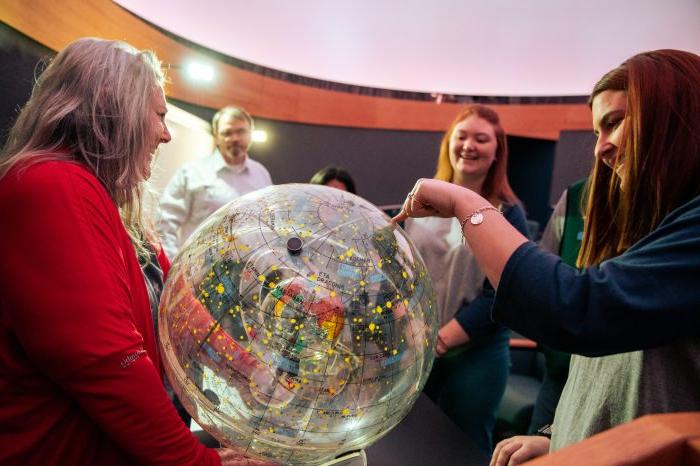 A group of females looking at an orb solar system.